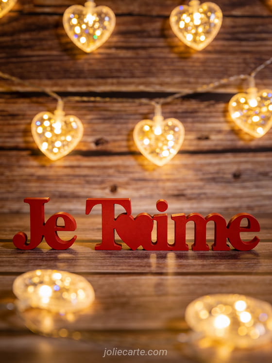 Guirlandes lumineuses en forme de cœurs sur fond bois rustique avec texte rouge Je T'aime