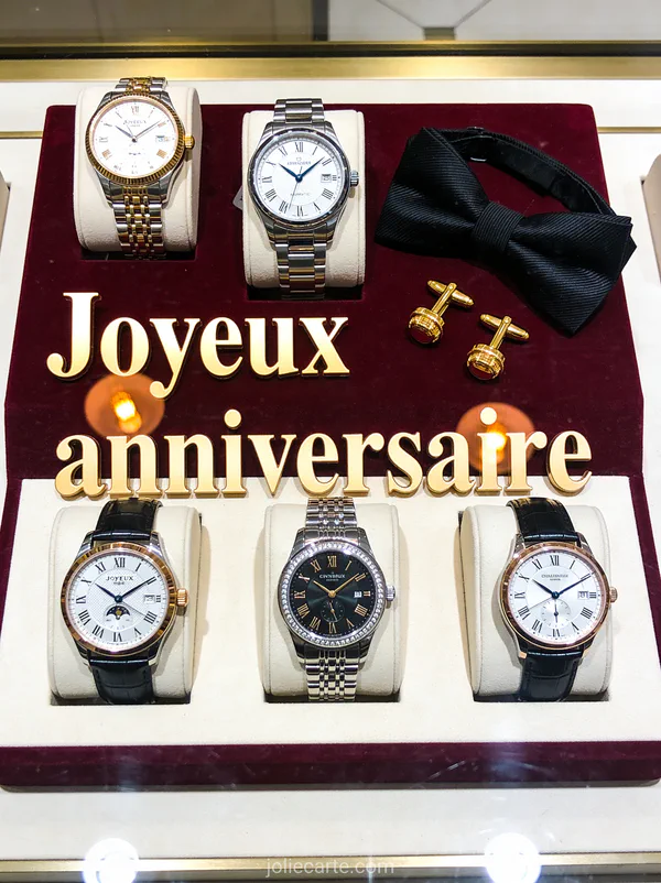 Montres de luxe sur présentoir en velours bordeaux avec boutons de manchette et nœud papillon et le texte Joyeux anniversaire