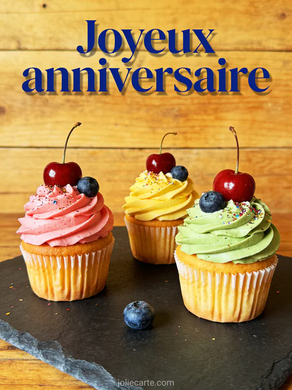 Cupcakes colorés décorés de crème chantilly et fruits sur plateau ardoise avec le texte Joyeux anniversaire