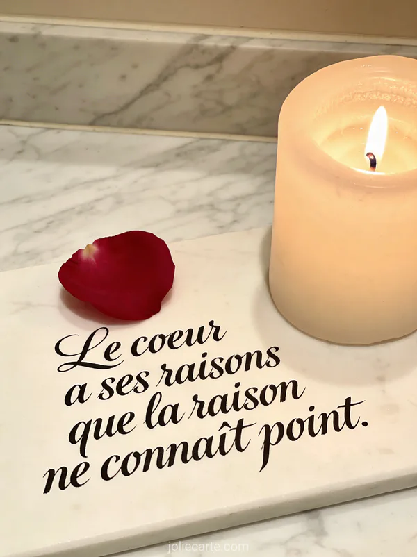 Cœur composé de pétales de roses rouges sur marbre blanc avec lumière de bougie et le texte Le cœur a ses raisons que la raison ne connaît point
