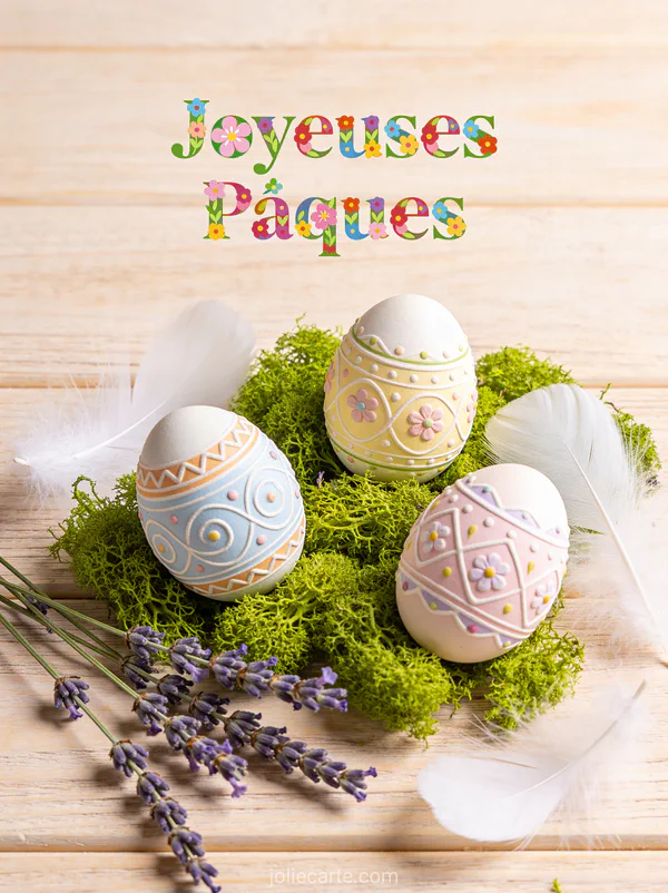 Composition de Pâques avec œufs peints à la main sur mousse verte, plumes blanches et brins de lavande sur fond bois clair, texte Joyeuses Pâques en lettres fleuries