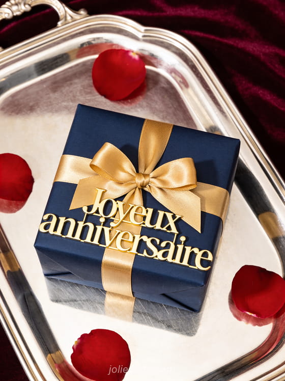 Texte Joyeux anniversaire en lettres dorées en relief classiques avec cadeau élégant en papier bleu nuit et noeud doré, pétales de rose sur velours bordeaux