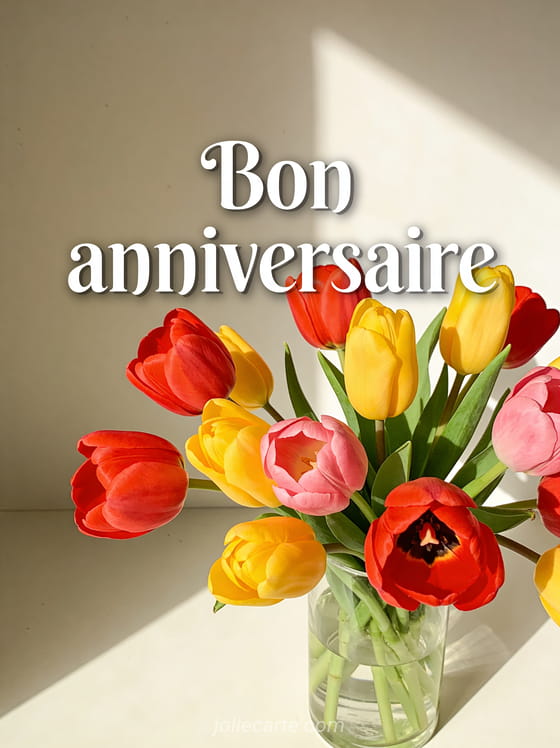 Texte Bon anniversaire en lettres blanches élégantes avec un bouquet de tulipes multicolores dans un vase en verre et lumière du matin
