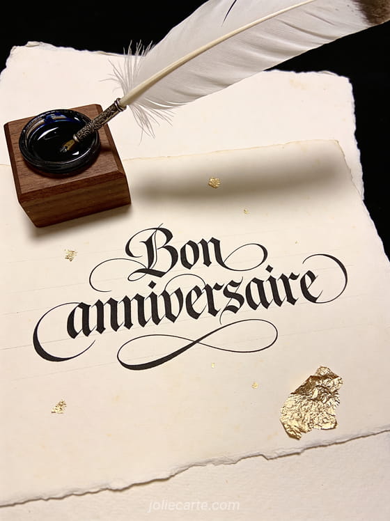 Texte Bon anniversaire en calligraphie à la plume avec encre noire sur papier vélin ivoire touches de feuille d'or et encrier