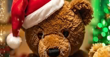 Cartão animado de Natal com uma família de ursos de pelúcia com gorros de Pai Natal, reunidos à volta de uma mesa com chá e biscoitos, num ambiente acolhedor e festivo.