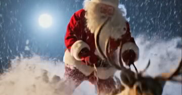 O Pai Natal, com um ar apressado, monta uma rena que corre velozmente por uma paisagem noturna coberta de neve, sob a luz da lua.