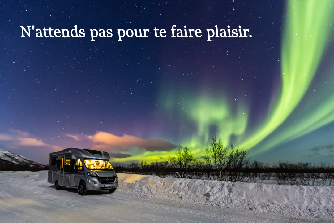 Un camping-car illuminé est stationné sur une route enneigée, sous un ciel nocturne rempli d'étoiles et de magnifiques aurores boréales vertes.