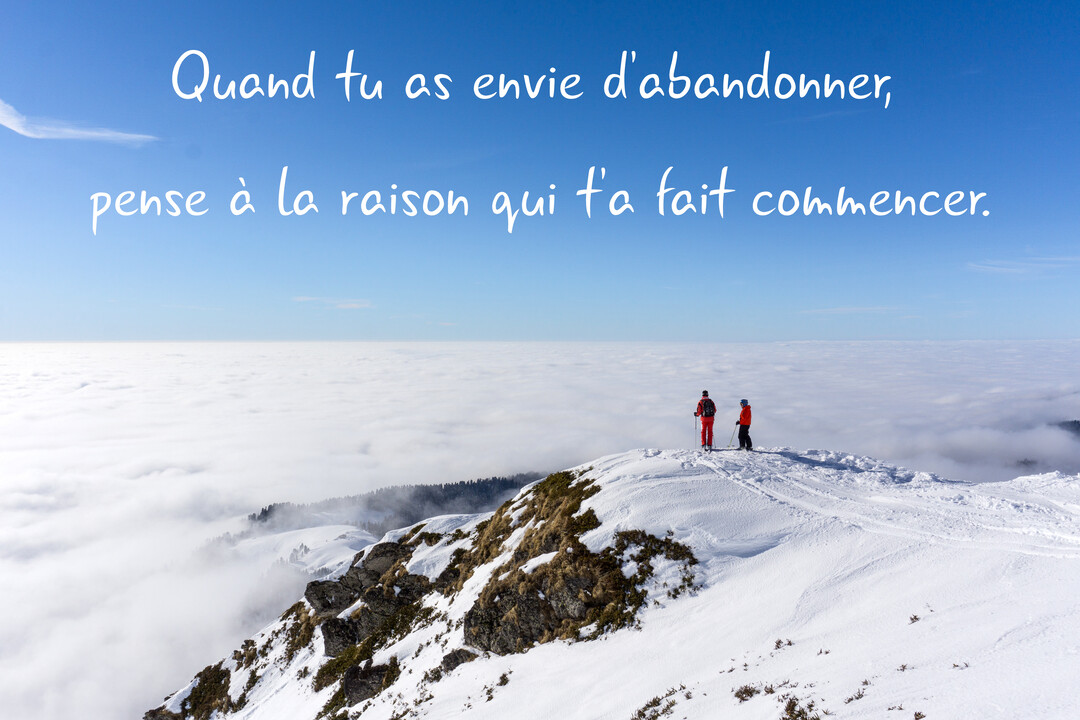 Deux personnes en tenue de randonnée hivernale se tiennent au sommet d'une montagne couverte de neige, admirant un vaste paysage de nuages.