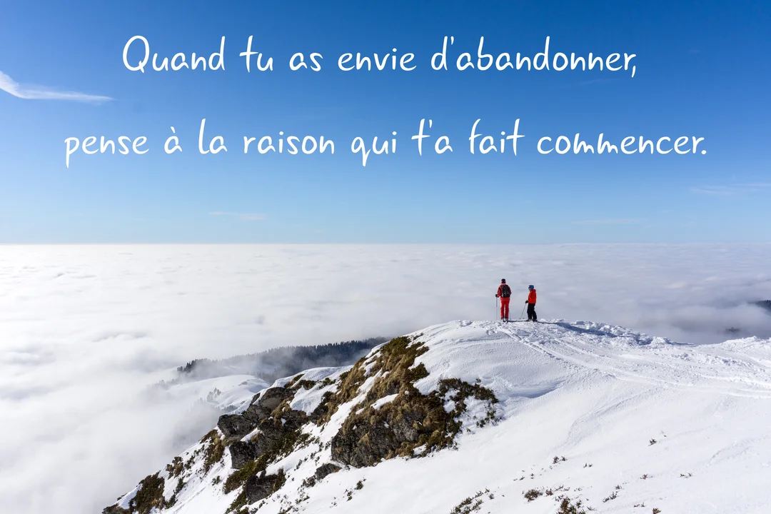Deux personnes en tenue de randonnée hivernale se tiennent au sommet d'une montagne couverte de neige, admirant un vaste paysage de nuages.