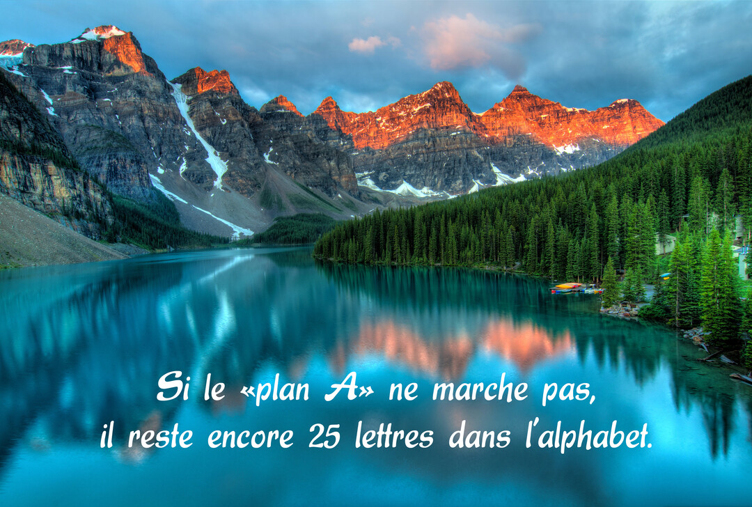 Un lac de montagne turquoise reflète des sommets enneigés et éclairés par le soleil couchant, avec une forêt de sapins sur la rive.