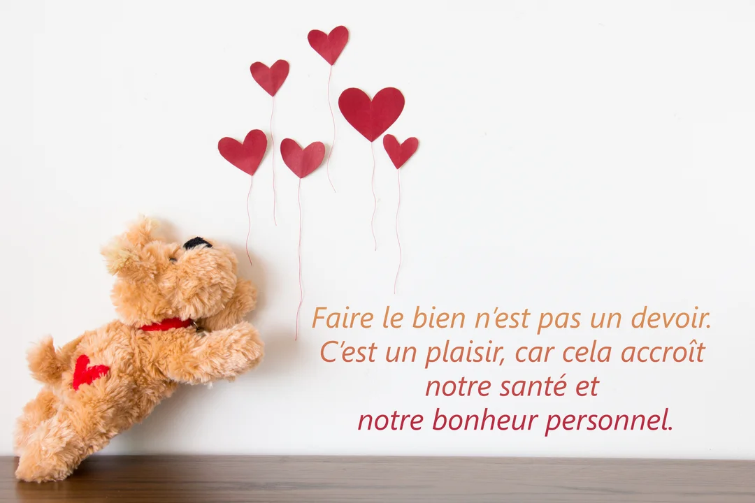 Un ourson en peluche marron est allongé sur une surface en bois, semblant poursuivre des ballons en forme de cœur rouges sur un fond blanc.