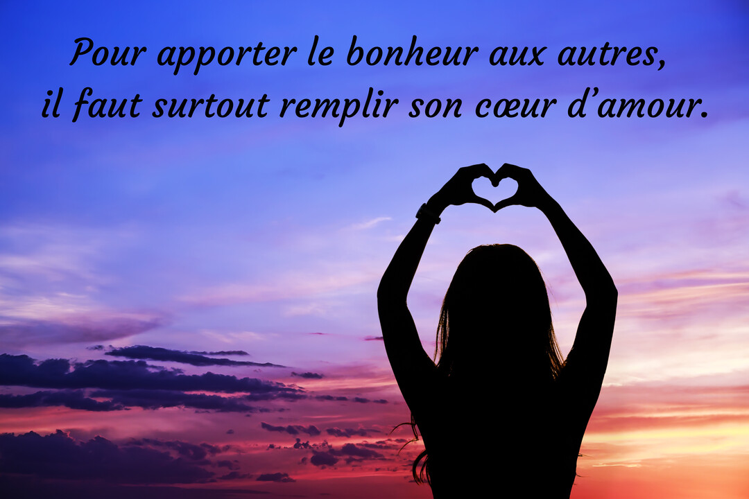 Vue de dos, la silhouette d'une femme forme un cœur avec ses mains au-dessus de sa tête devant un ciel crépusculaire violet et rose.