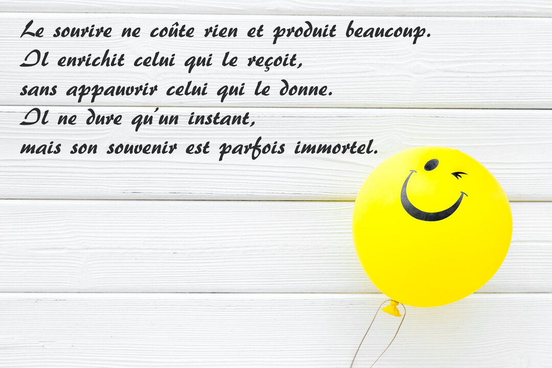 Sur un fond de planches de bois blanches, une citation sur le sourire est écrite en noir, accompagnée d'un ballon jaune smiley.