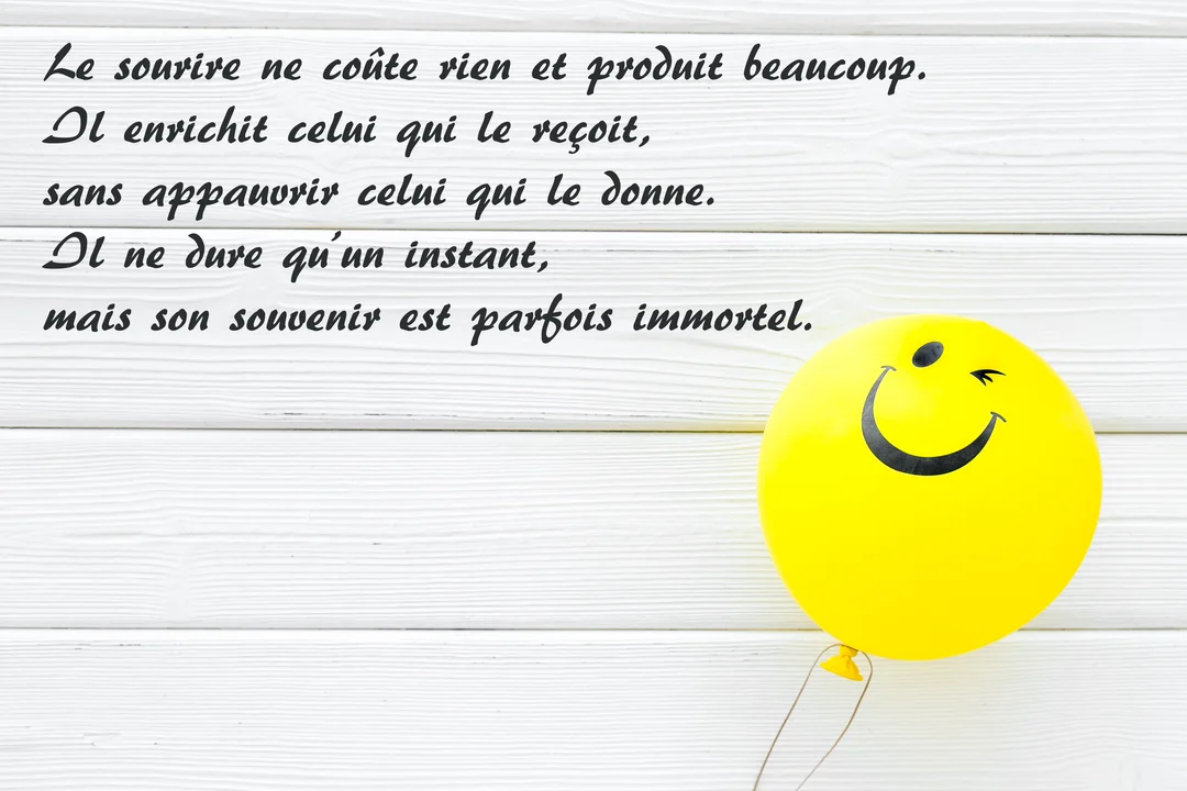 Sur un fond de planches de bois blanches, une citation sur le sourire est écrite en noir, accompagnée d'un ballon jaune smiley.