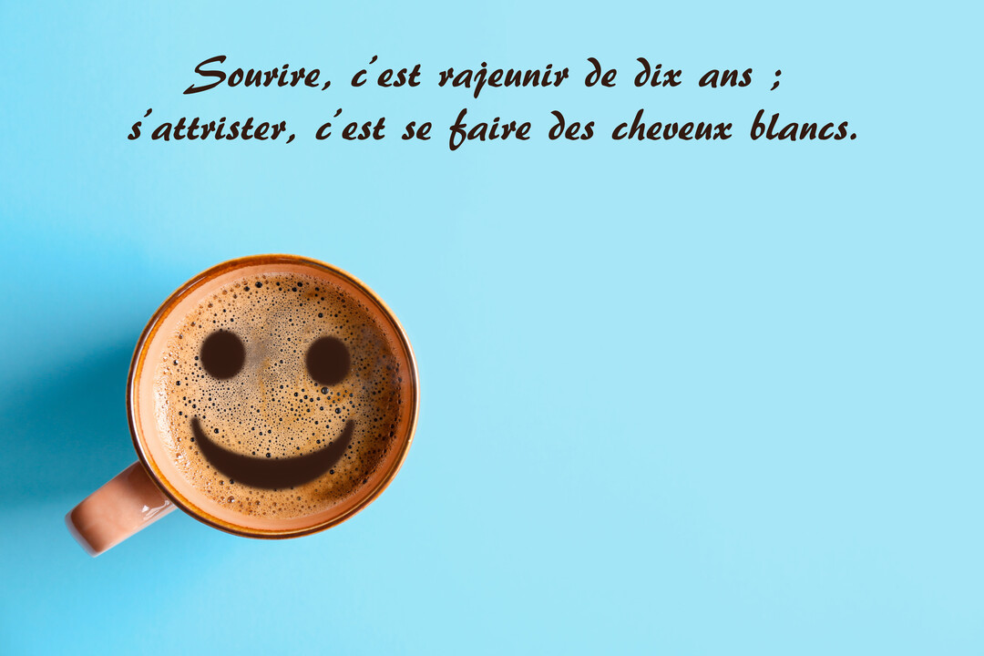 Vue de dessus d'une tasse de café sur fond bleu, avec un grand visage souriant dessiné dans la mousse onctueuse du café.