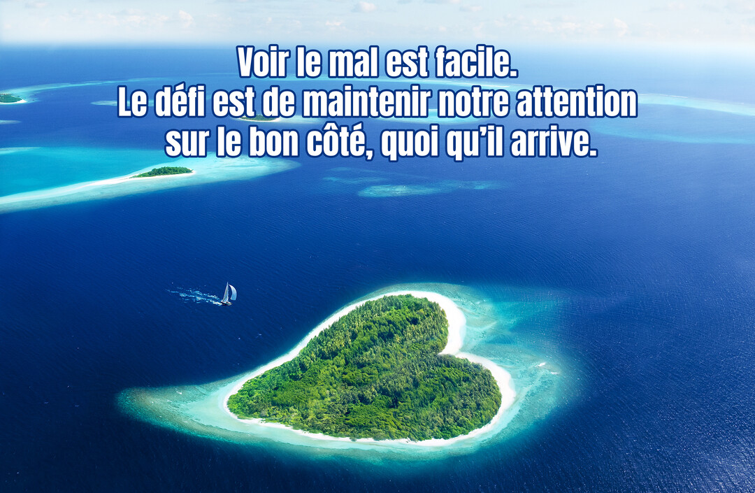 Vue aérienne d'une luxuriante île tropicale en forme de cœur et d'un voilier naviguant sur une mer d'un bleu profond et limpide.