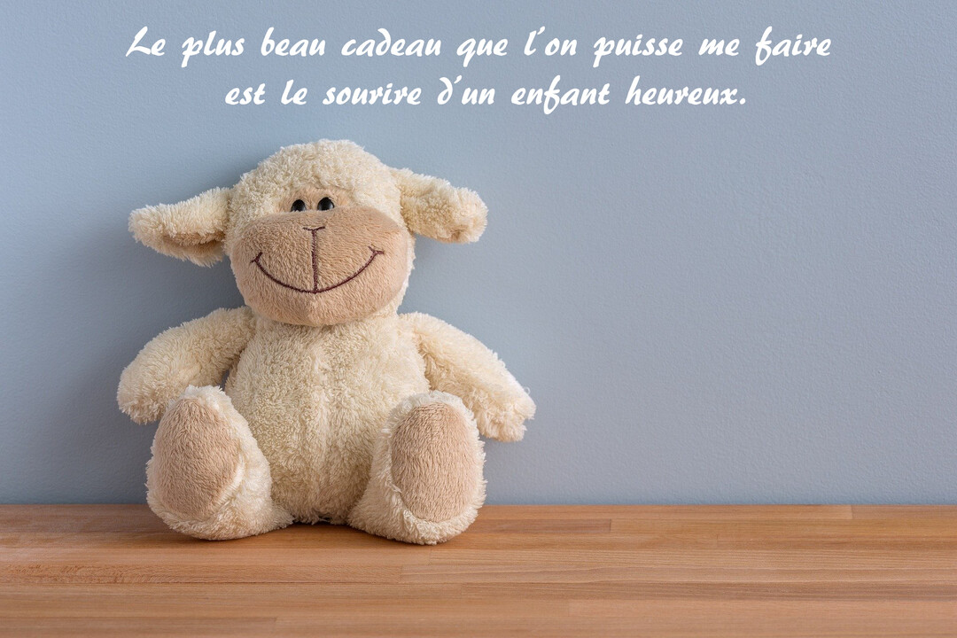 Une peluche de mouton de couleur crème, assise et souriante, est posée sur une étagère en bois devant un mur bleu-gris uni.
