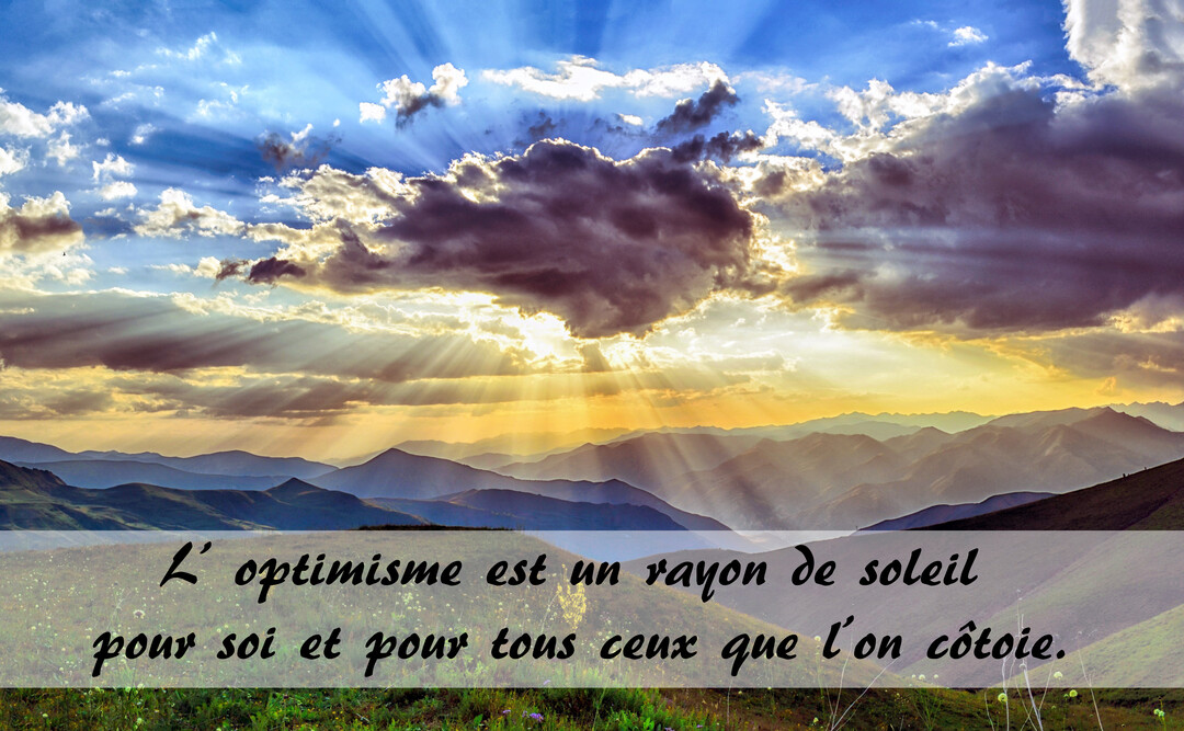 Un ciel nuageux est percé de rayons de soleil dorés qui illuminent une chaîne de montagnes en contrebas, créant une scène inspirante.