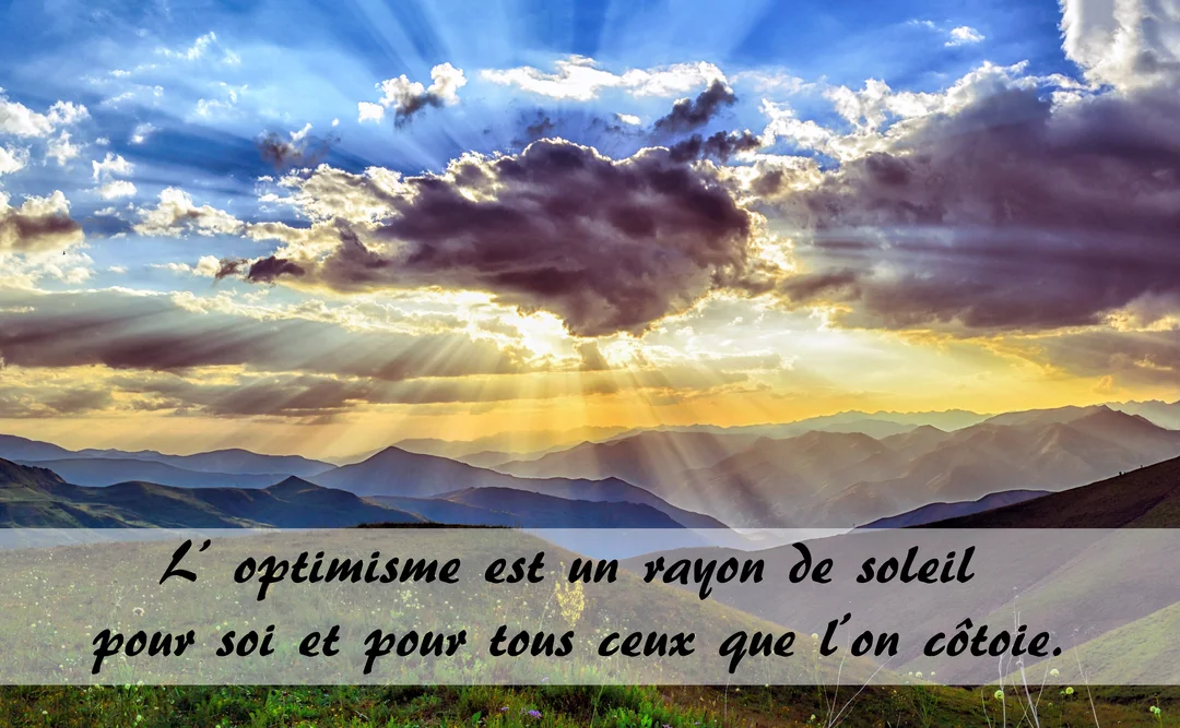 Un ciel nuageux est percé de rayons de soleil dorés qui illuminent une chaîne de montagnes en contrebas, créant une scène inspirante.