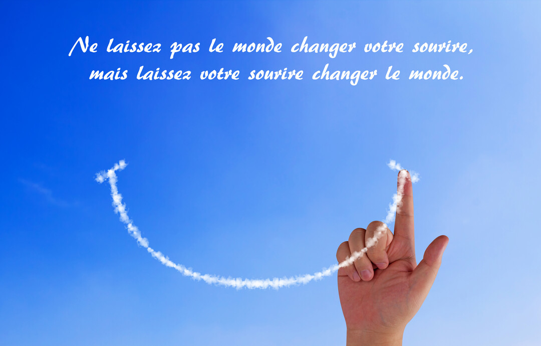Sur un fond de ciel bleu azur, une main trace du bout de l'index un smiley souriant avec un nuage blanc vaporeux.