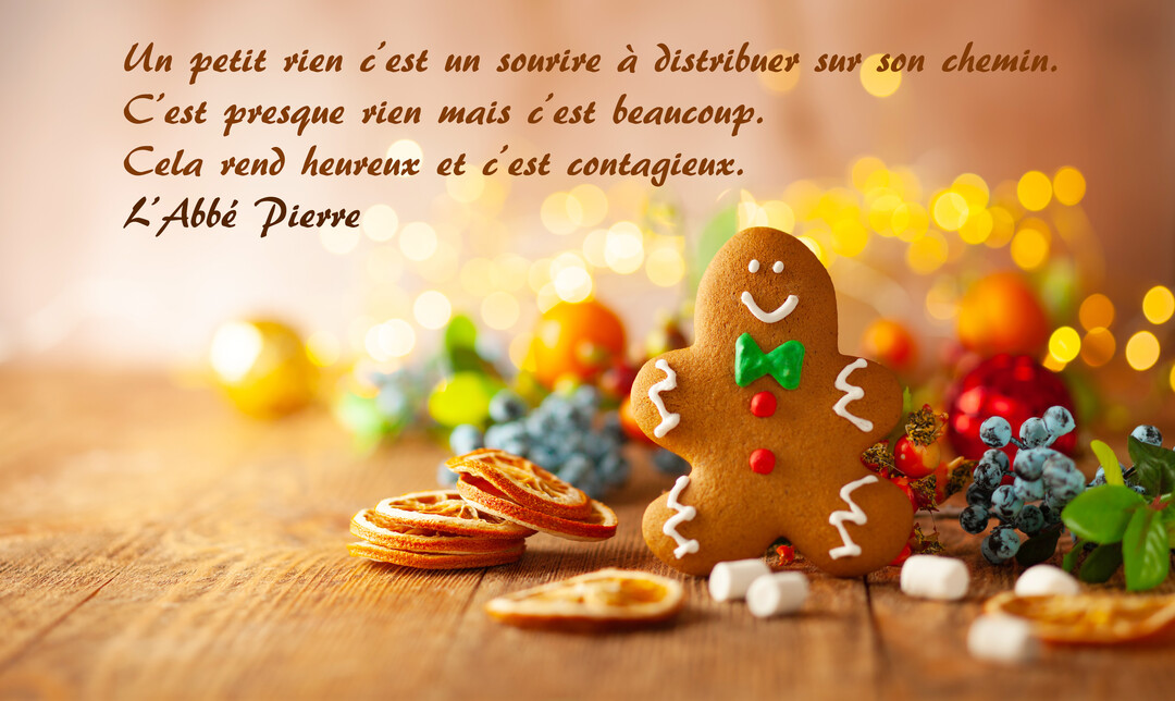 Un bonhomme en pain d'épices souriant est posé sur une table en bois avec des décorations festives et des lumières floues en arrière-plan.