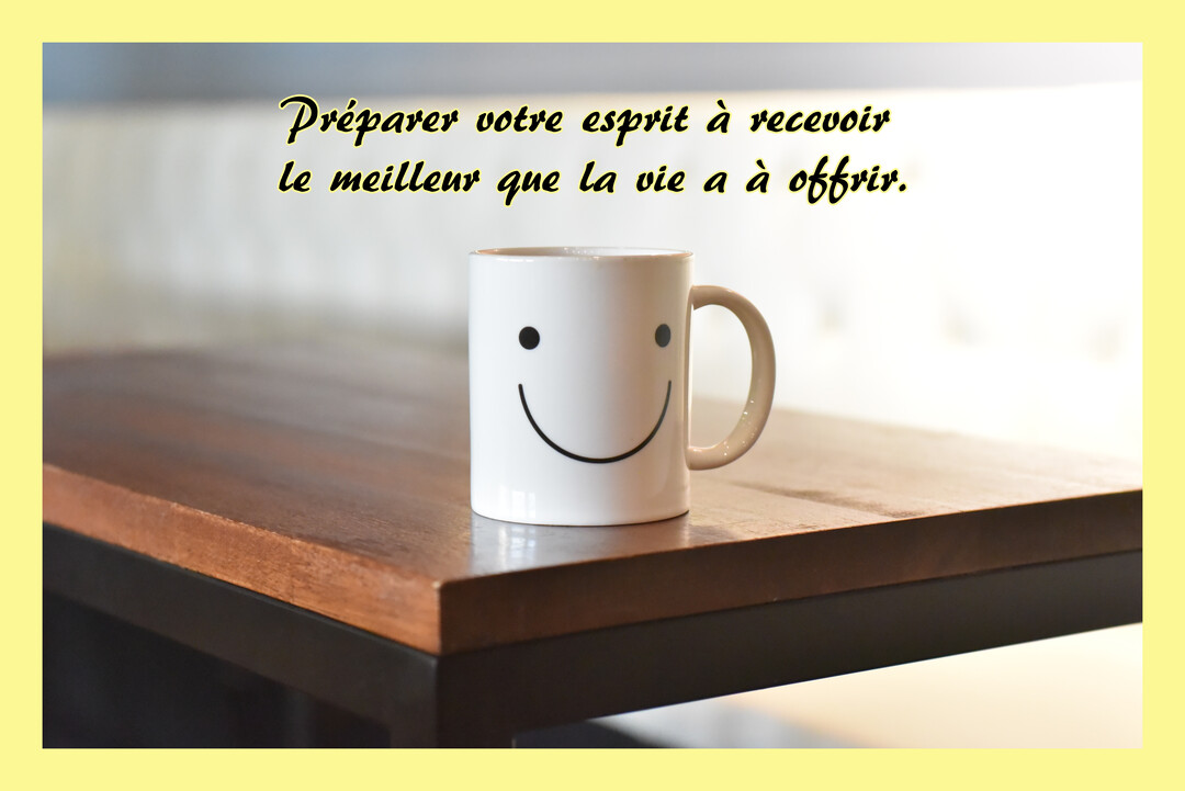 Une tasse blanche avec un smiley souriant est posée sur une table en bois, sur un fond lumineux, illustrant un message d'optimisme.