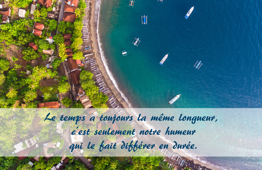 Vue plongeante d'un littoral tropical luxuriant, où des bateaux flottent sur une mer turquoise à côté d'une plage de sable fin.