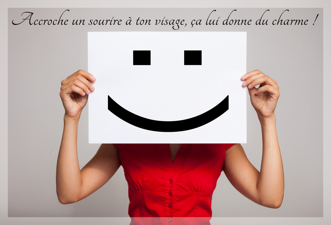Une femme portant une chemise rouge cache son visage derrière une feuille de papier sur laquelle est dessiné un grand smiley noir.