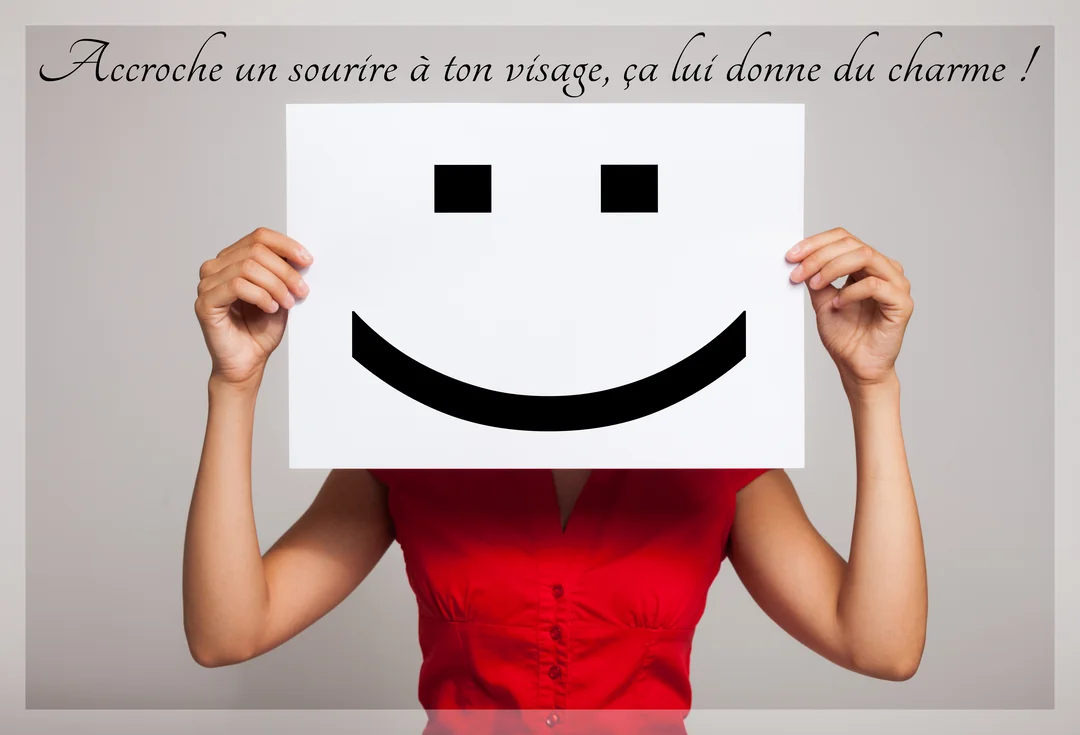 Une femme portant une chemise rouge cache son visage derrière une feuille de papier sur laquelle est dessiné un grand smiley noir.