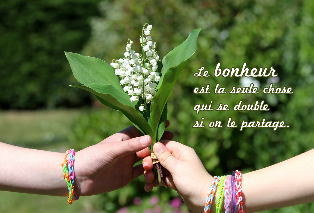 Deux jeunes mains parées de bracelets multicolores se passent un petit bouquet de muguet sur un fond de verdure ensoleillée et floue.