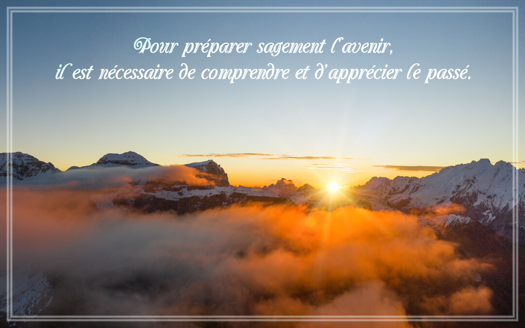 Un soleil éclatant se lève sur une chaîne de montagnes enneigées, illuminant des nuages bas d'une lueur orangée sous un ciel bleu.