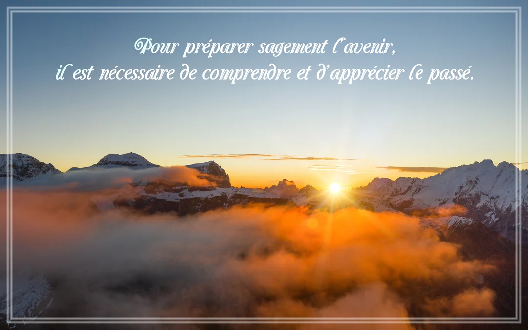 Un soleil éclatant se lève sur une chaîne de montagnes enneigées, illuminant des nuages bas d'une lueur orangée sous un ciel bleu.