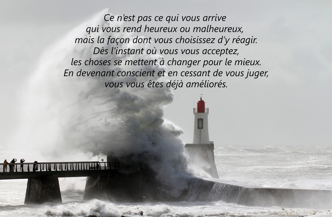 Une photographie impressionnante montrant une vague gigantesque qui déferle sur une jetée, à côté d'un phare blanc et rouge sous un ciel gris.