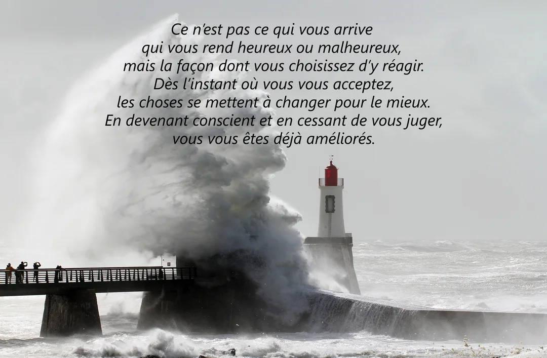 Une photographie impressionnante montrant une vague gigantesque qui déferle sur une jetée, à côté d'un phare blanc et rouge sous un ciel gris.