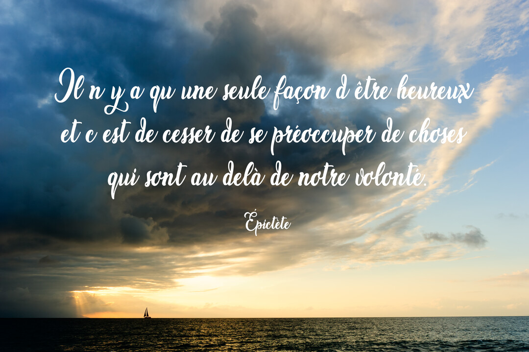 Un voilier navigue sur une mer calme au coucher du soleil, sous un ciel chargé de nuages sombres et de lumière dorée.