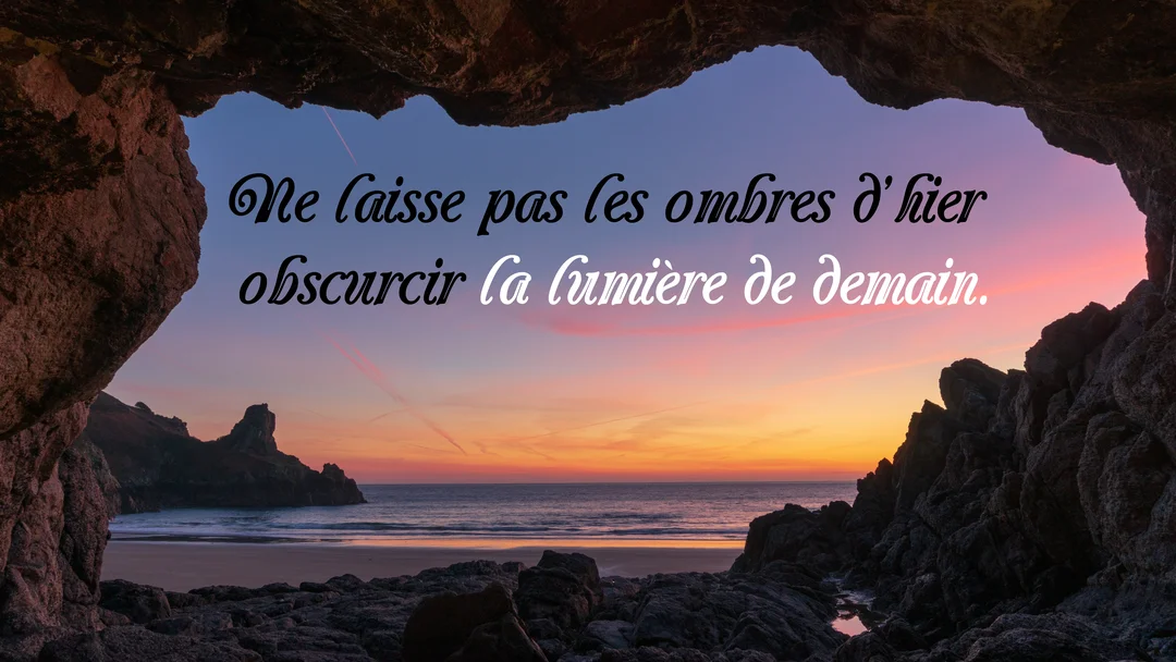 Vue depuis l'intérieur d'une grotte rocheuse, un coucher de soleil sur l'océan illumine le ciel de teintes orange et roses.