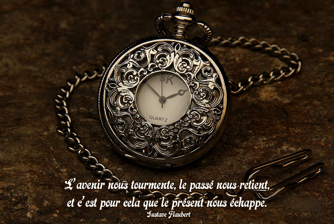 Une montre à gousset vintage en argent, richement décorée, posée avec sa chaîne sur une surface rocheuse texturée de couleur sombre.
