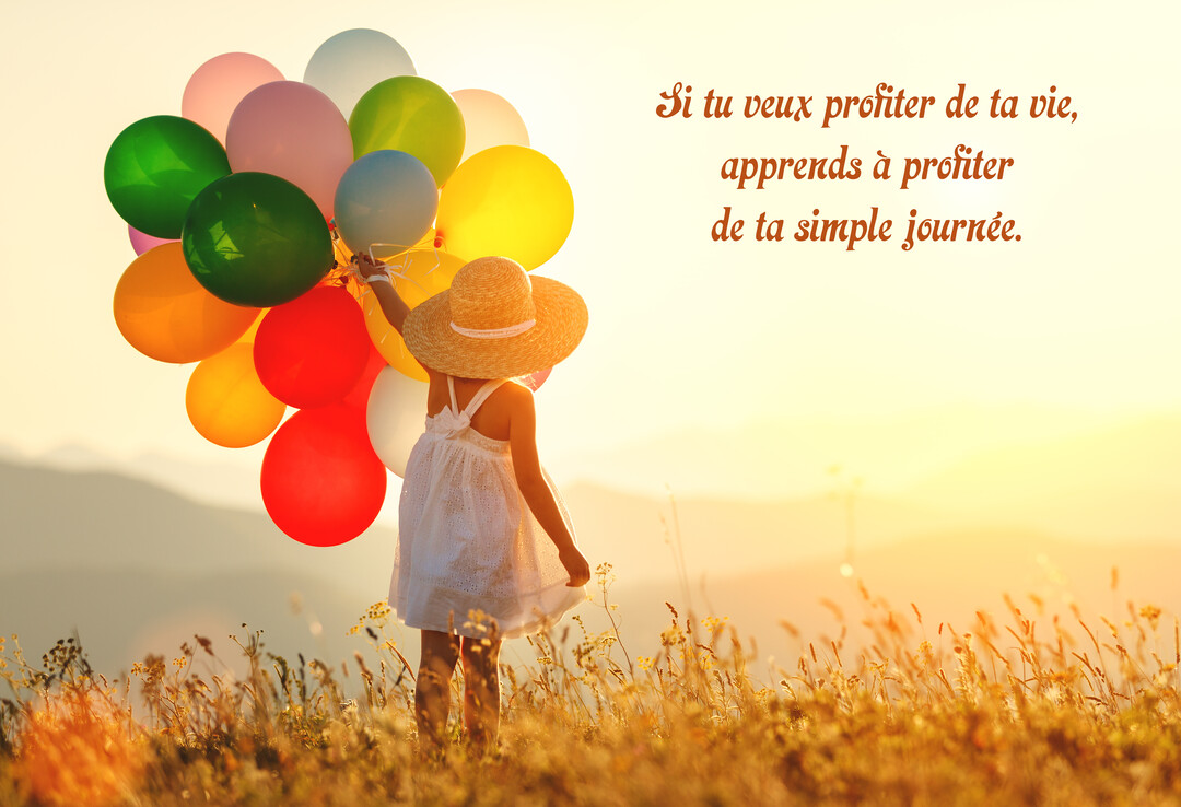 Vue de dos d'une enfant en robe blanche et chapeau de paille, tenant une grappe de ballons multicolores dans un pré ensoleillé.