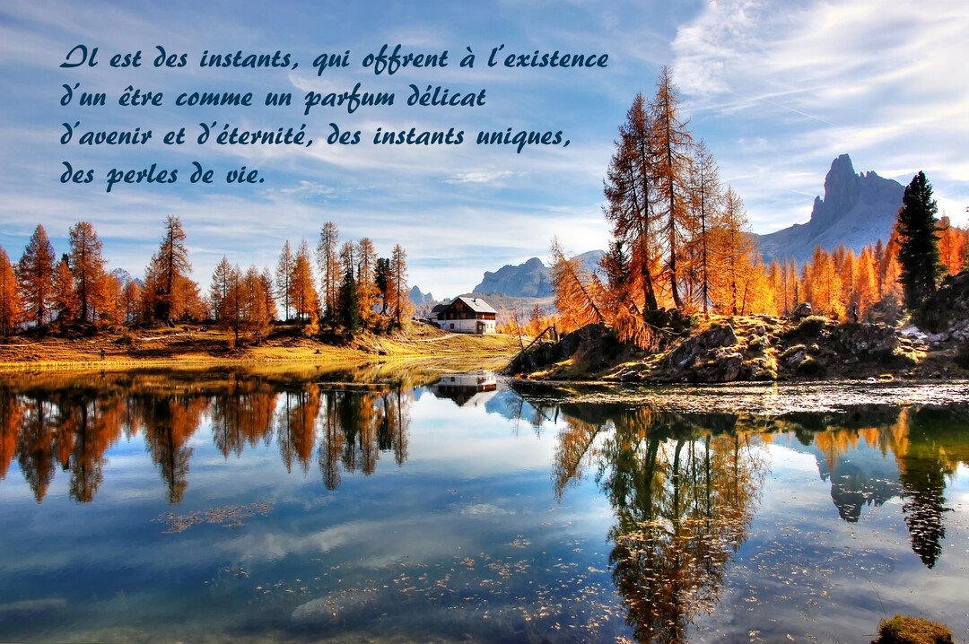 Un lac de montagne en automne reflète une forêt de mélèzes dorés et un chalet, sous un ciel bleu parsemé de nuages.
