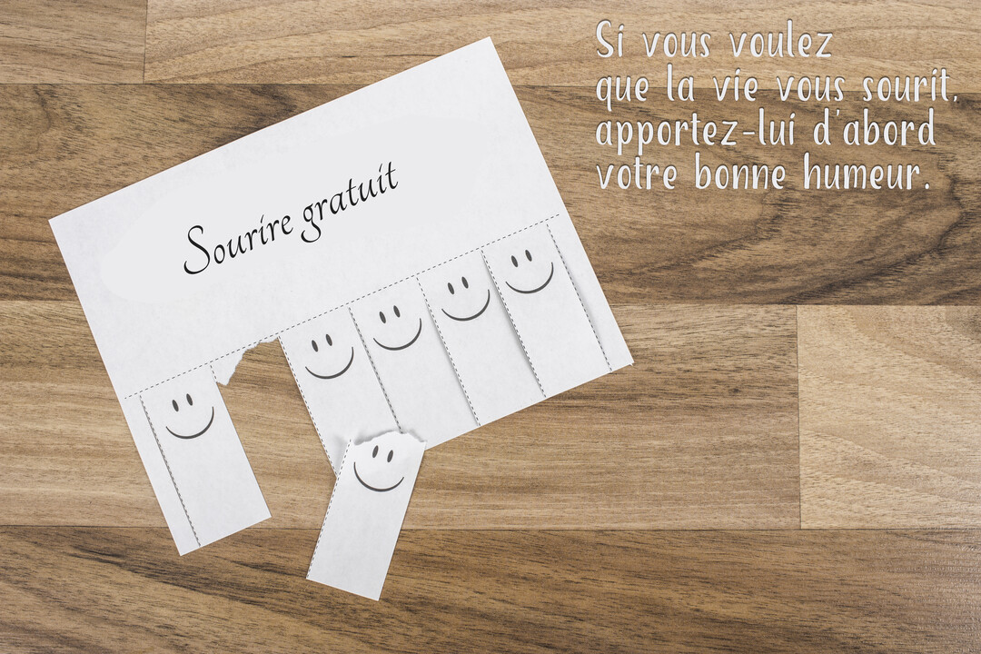 Sur un fond en bois, une annonce en papier offre des 'sourires gratuits' sur des languettes détachables, accompagnée d'une citation sur la bonne humeur.