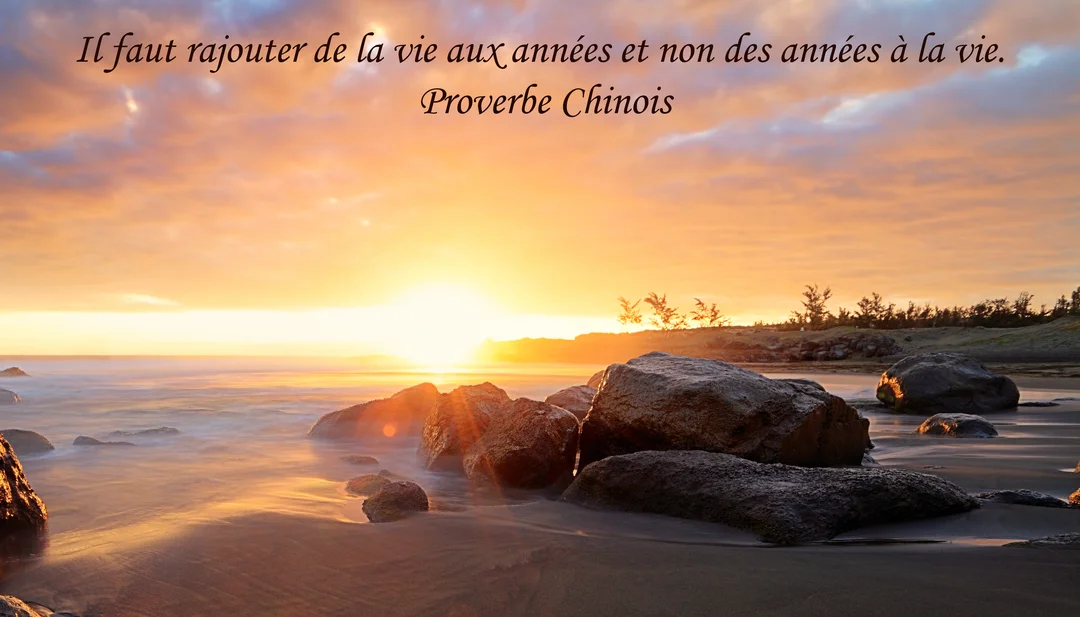 Un paysage marin au crépuscule, avec le soleil se couchant à l'horizon derrière des rochers sombres sur une plage de sable mouillé.