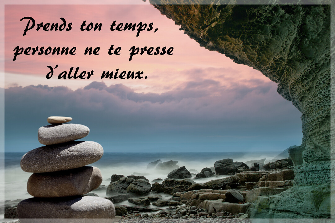 Un empilement de galets en équilibre sur une plage rocheuse, avec une mer brumeuse et un ciel aux teintes pastel en arrière-plan.