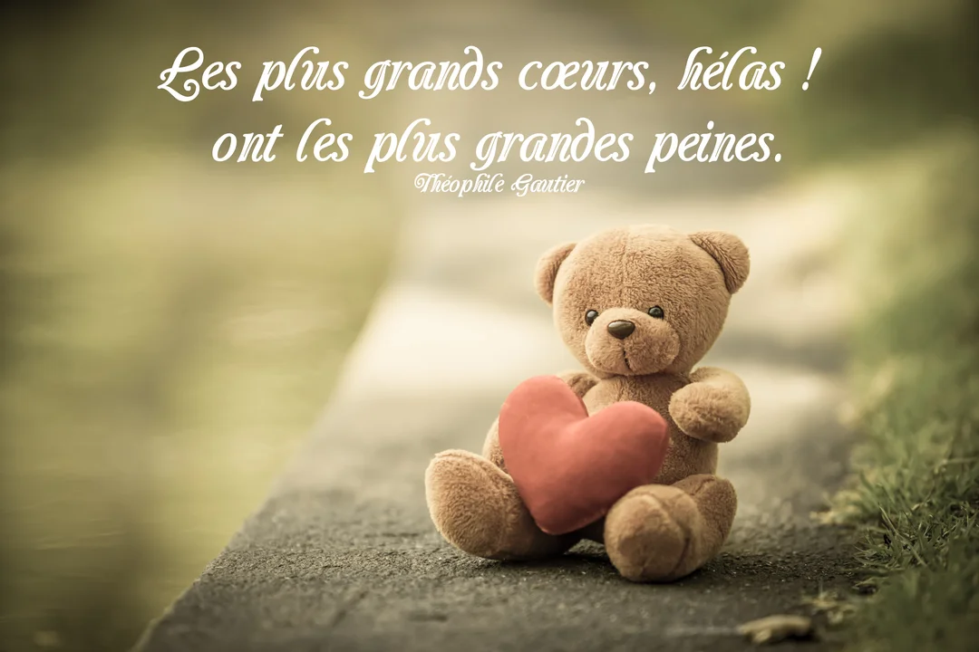 Un petit ours en peluche marron est assis sur une surface en pierre, tenant un cœur en tissu rouge, sur un arrière-plan flou.