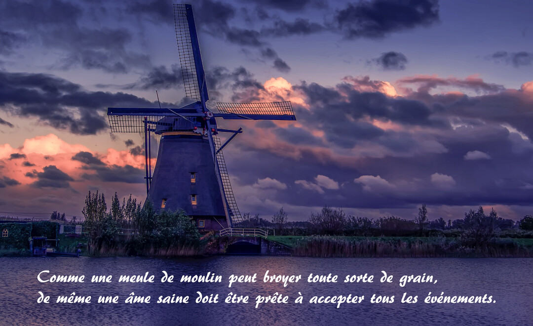 Un moulin à vent traditionnel se dresse au bord d'un canal sous un ciel dramatique aux couleurs du crépuscule, avec des nuages violets et roses.