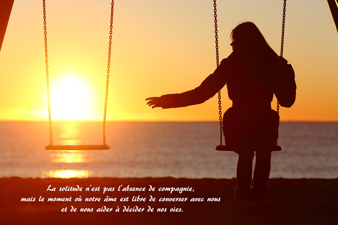 Une silhouette de femme assise sur une balançoire sur la plage regarde une balançoire vide à côté d'elle, face à un coucher de soleil sur l'océan.