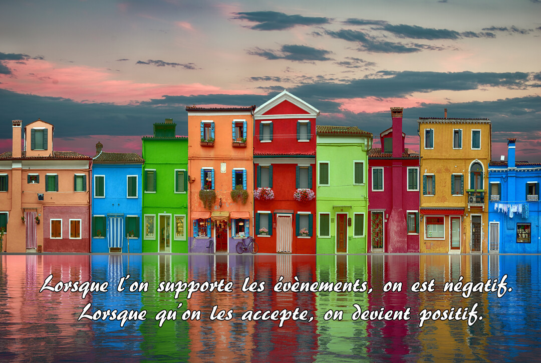Des façades de maisons de toutes les couleurs sont alignées au bord de l'eau, sous un ciel nuageux aux teintes roses.