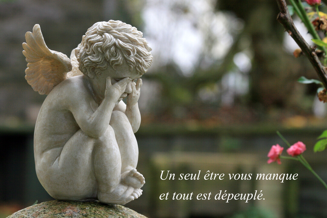 Une statue de pierre représentant un ange recroquevillé qui pleure dans ses mains, posée sur un rocher dans un jardin verdoyant.