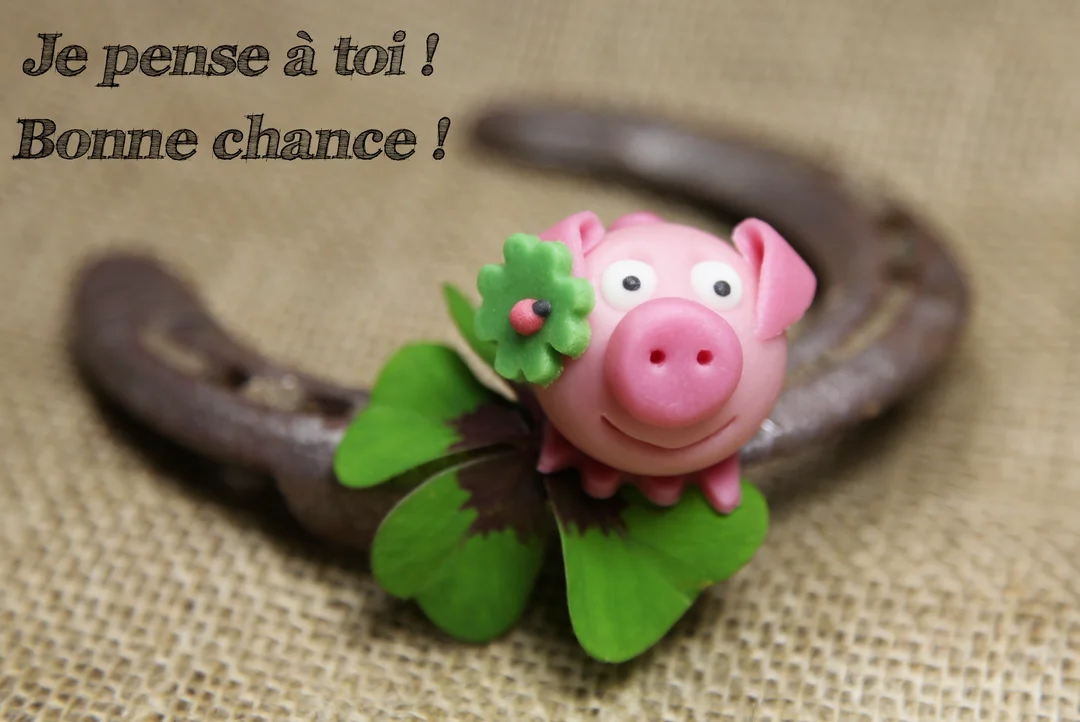 Une figurine rose en forme de cochon sourit, tenant un trèfle à quatre feuilles, avec un fer à cheval rouillé en arrière-plan.