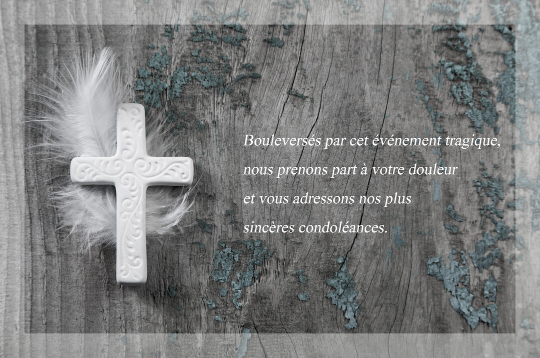 Une croix en céramique blanche aux motifs délicats repose sur de fines plumes blanches, le tout sur une planche de bois rustique grisâtre.