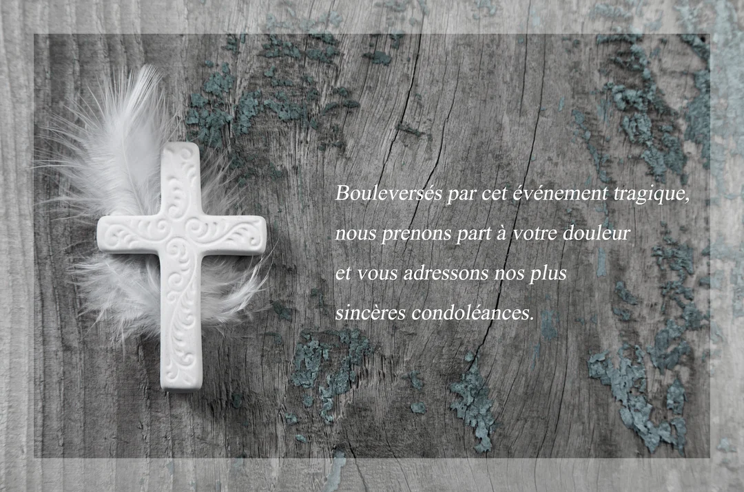 Une croix en céramique blanche aux motifs délicats repose sur de fines plumes blanches, le tout sur une planche de bois rustique grisâtre.
